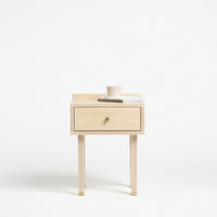 Light wood nightstand with a minimalist design, featuring a simple drawer and natural finish, set against a white background.