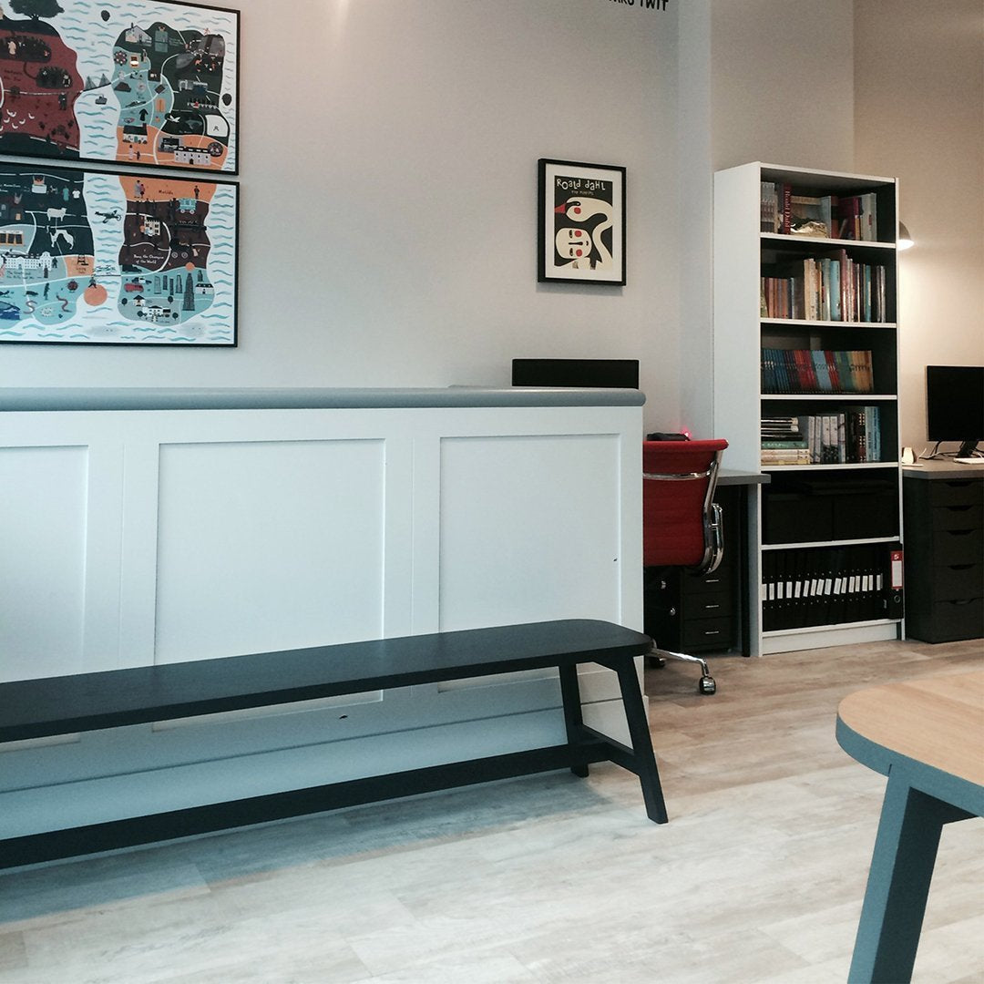 Modern black bench with a sleek design, set against light wood floors and minimalist white walls.