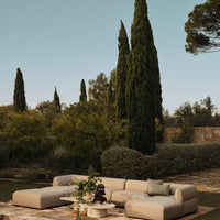 Beige sectional sofa with subtle texture, set against a backdrop of lush greenery and towering trees.