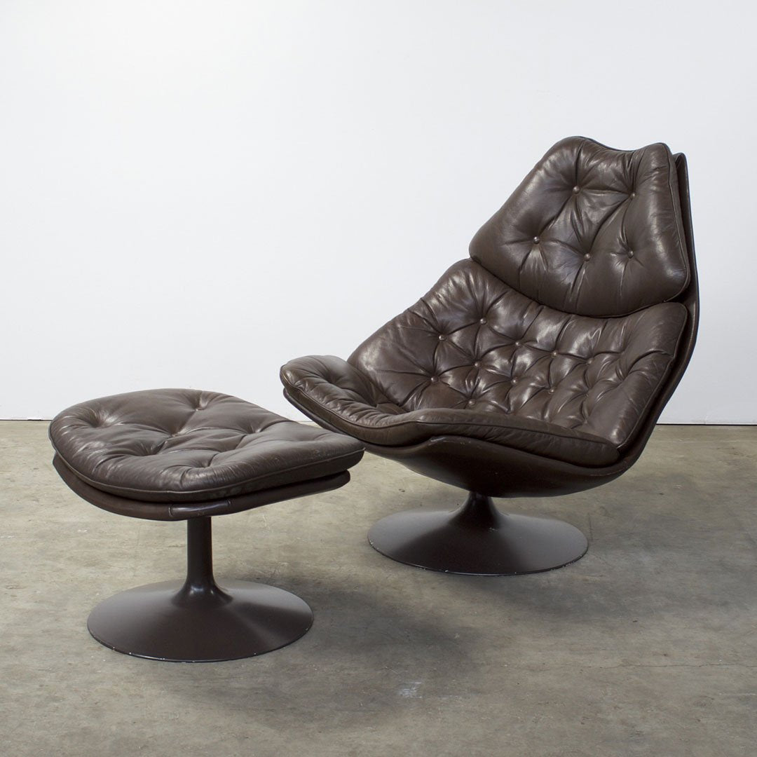 Brown leather armchair with tufted cushion design and matching ottoman, featuring a sleek, modern silhouette.