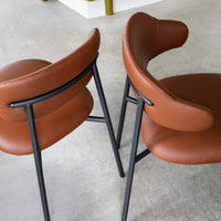 Brown leather chairs with a smooth finish and black metal frames, featuring a modern, minimalist design.