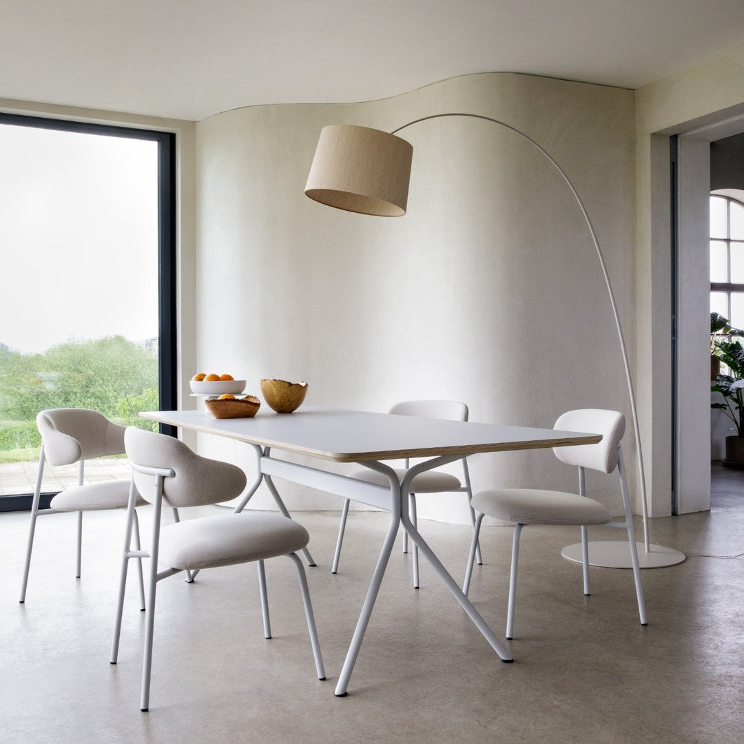Modern white dining table with soft beige chairs and a matching floor lamp, set against a neutral wall and greenery backdrop.