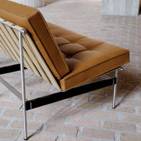 Tan tufted leather sofa with sleek metal frame and minimalist design, set against a textured brick floor.