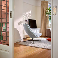 Light blue modern chair, warm wood flooring, neutral beige walls, layered textures, and soft green plants.