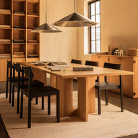 Light wood dining table with black chairs, neutral tones, and metallic pendant lights against a warm, minimalistic backdrop.