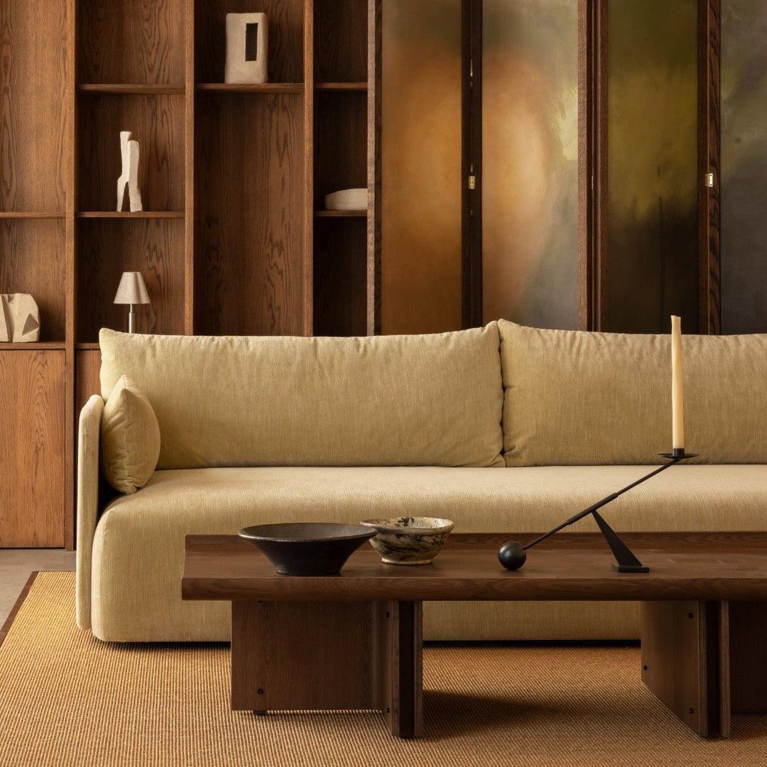Light olive green sofa against a warm wood backdrop, featuring smooth textures and subtle earthy patterns.
