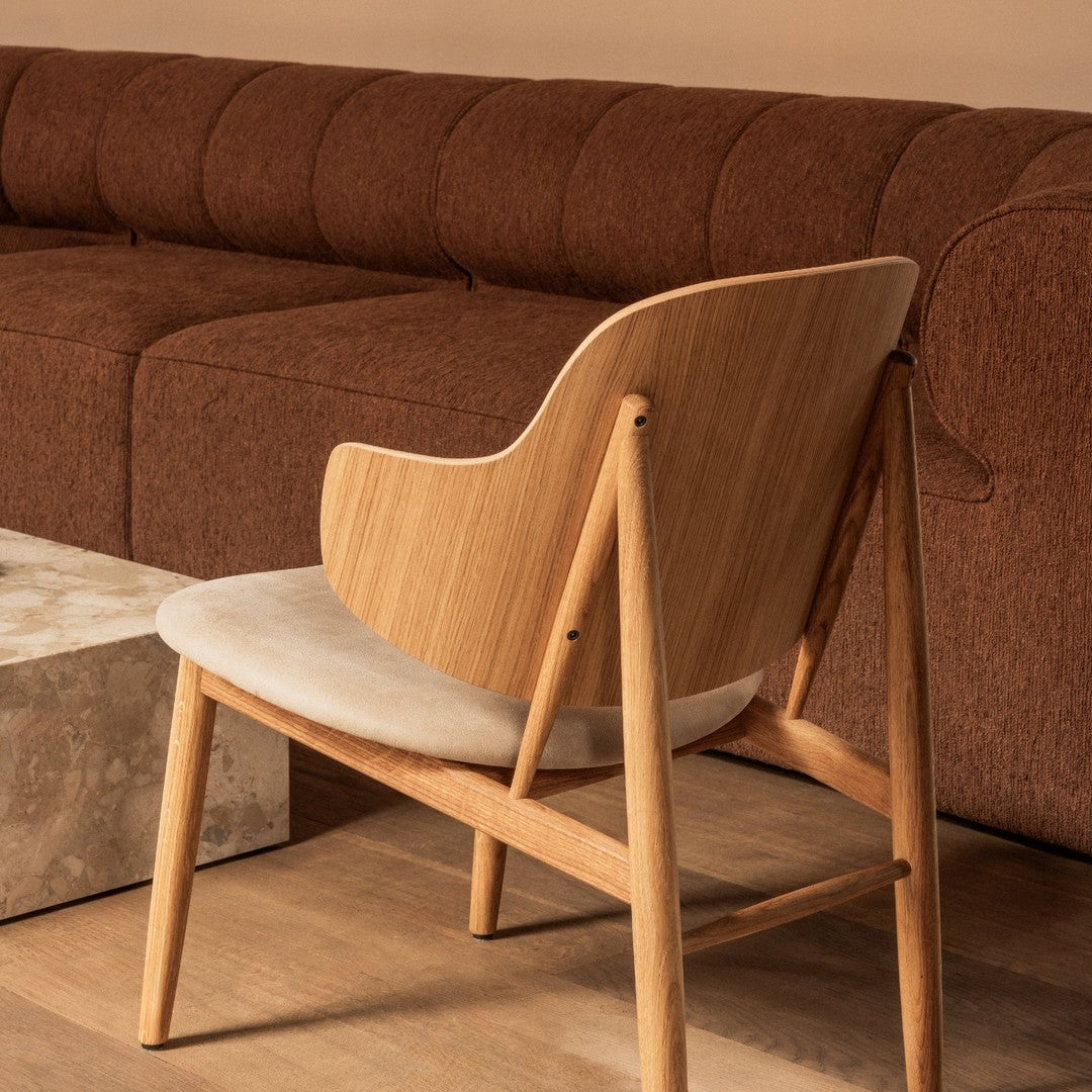 "Stylish wooden chair with cream upholstery, complemented by a rich brown couch and natural wood accents."