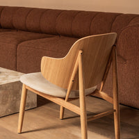 "Stylish wooden chair with cream upholstery, complemented by a rich brown couch and natural wood accents."