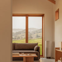 Cozy brown sofa in a warm-toned room with natural wood accents and soft, muted landscape views. Perfect for serene decor.
