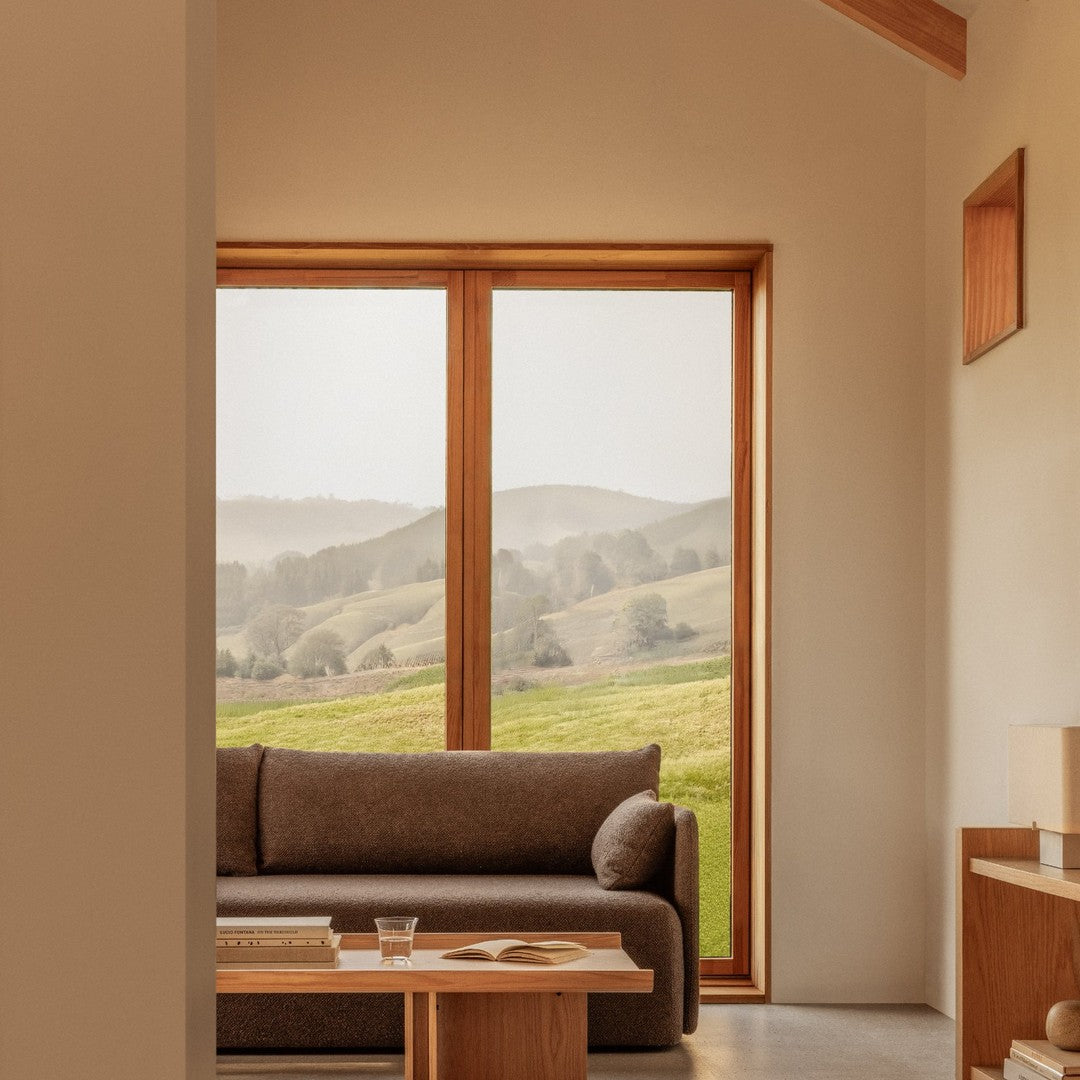 "Neutral-toned living room with a brown sofa, wooden accents, and a scenic view through large windows."