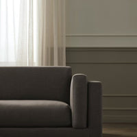 Gray upholstered sofa with a smooth texture, complemented by soft beige curtains and subtle wall paneling.