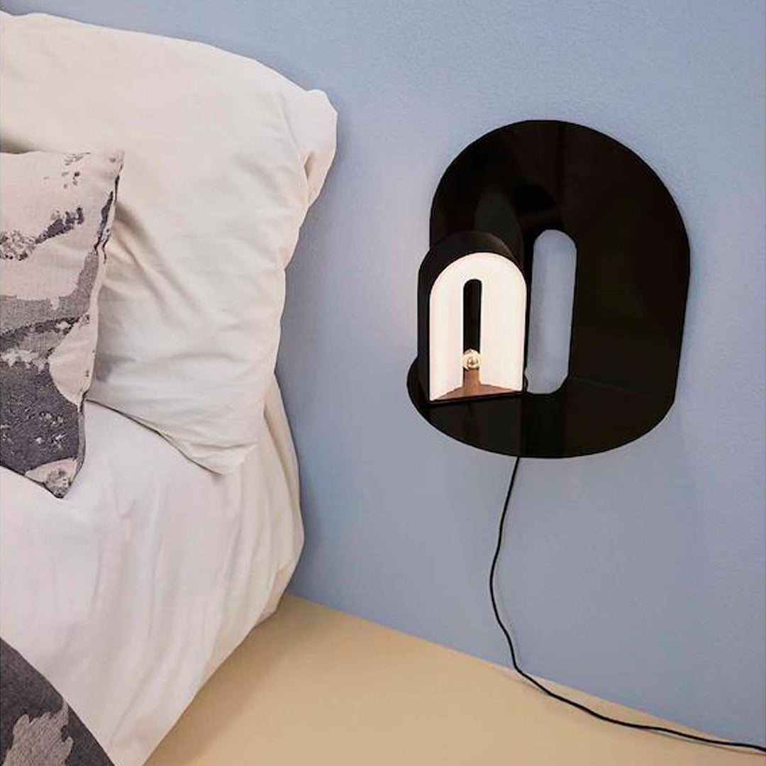 Black abstract wall lamp with a glossy finish and smooth lines against a soft blue wall, showcasing modern design.