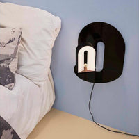 Black abstract wall lamp with a glossy finish and smooth lines against a soft blue wall, showcasing modern design.