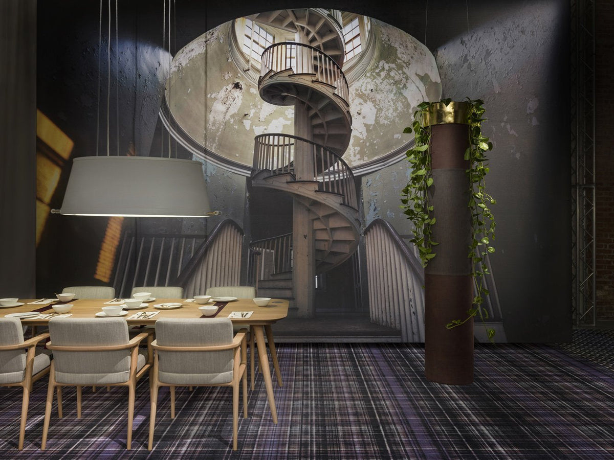 Spiral staircase mural with earthy tones, dark walls, and a plaid-patterned carpet in neutral colors.