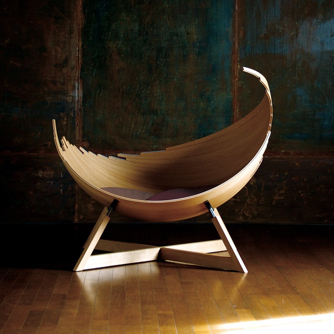 Natural wood finish with a smooth, curved design; complementary soft purple cushion against a textured backdrop.