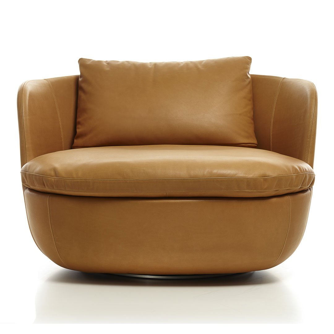Tan leather armchair with a smooth finish and rounded silhouette, featuring a cozy throw pillow.