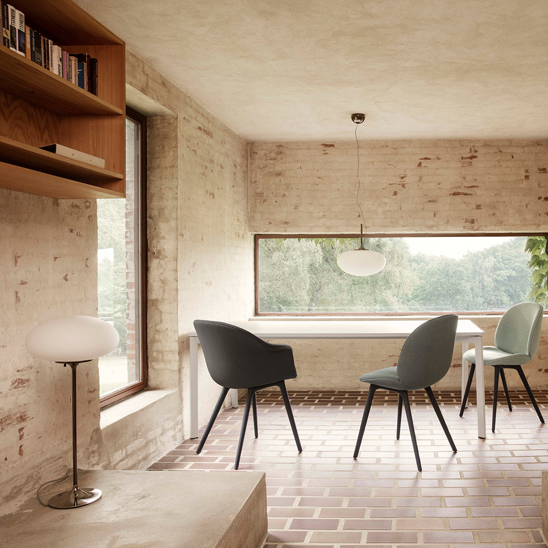 Minimalist dining room featuring grey and soft green chairs, warm brick flooring, and natural light.