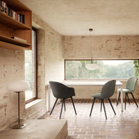 Minimalist dining room featuring grey and soft green chairs, warm brick flooring, and natural light.