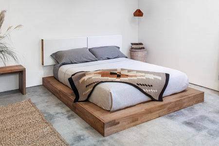 Bohemian-style blanket with earthy tones, geometric patterns on a cozy bed with gray bedding and wooden frame.