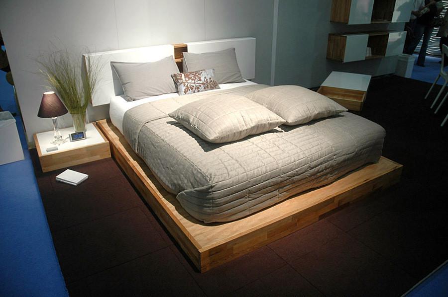 Modern bed with a neutral gray quilt, soft gray pillows, and wooden base, complemented by a dark brown rug.