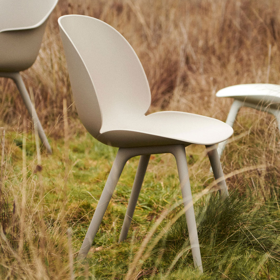 Light beige chair with a smooth finish, set against a natural grass backdrop. Simple and modern design.