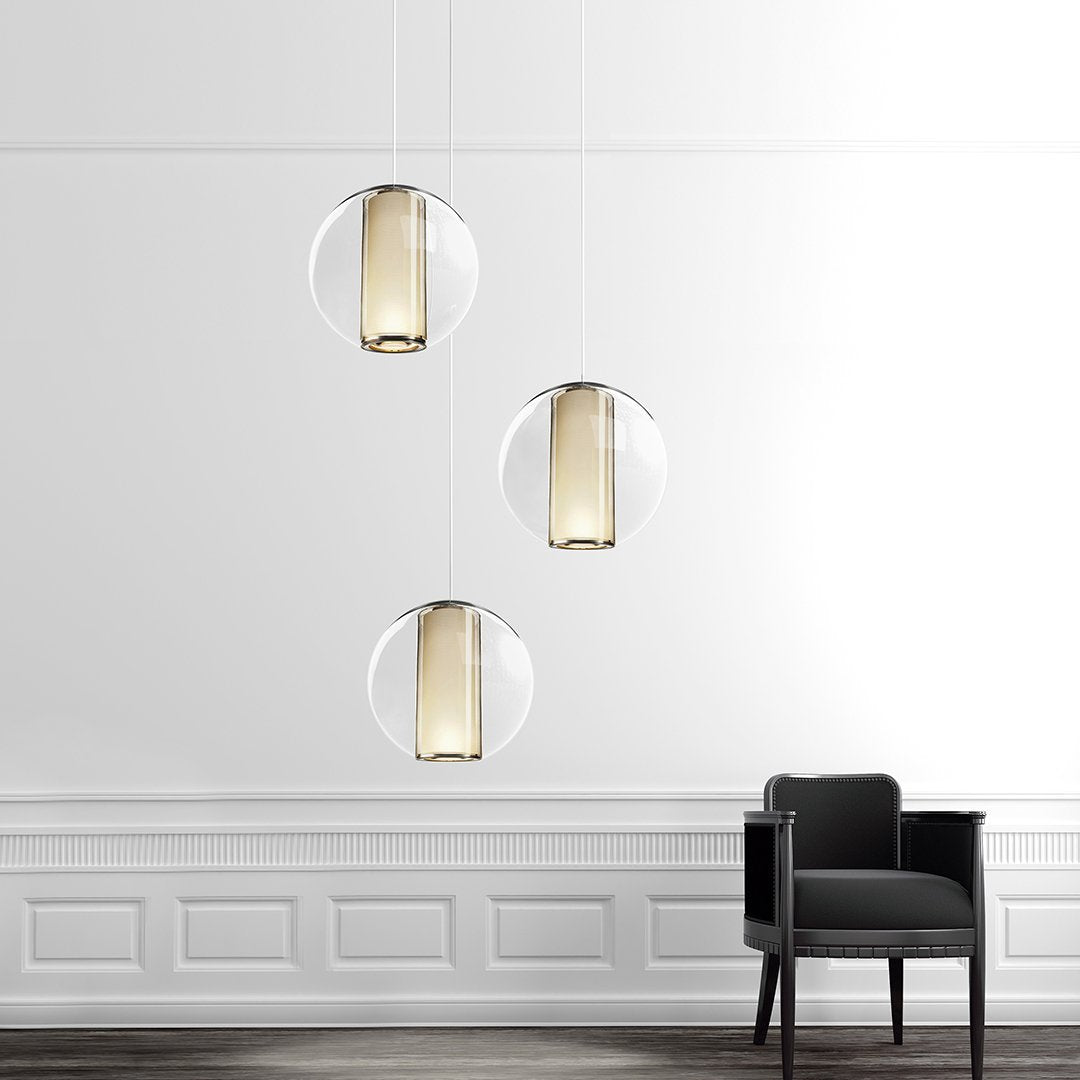 "Modern pendant lights featuring clear glass and warm gold accents, suspended against a white wall."