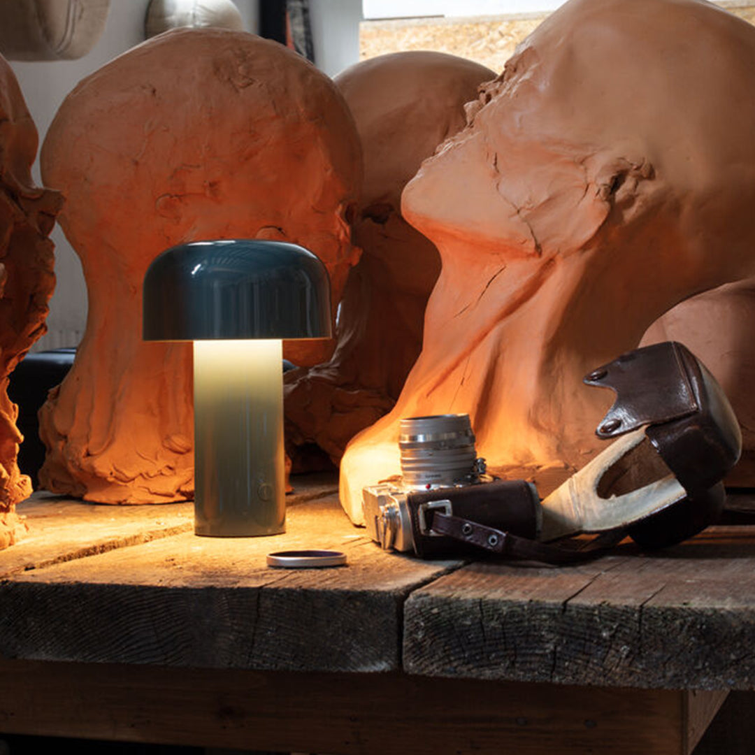 Green dome lamp with a frosted body, warm light casting a glow, surrounded by beige sculpted heads.
