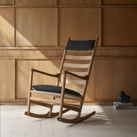 Light wood rocking chair with a natural finish and dark gray fabric cushion against a warm wooden backdrop.