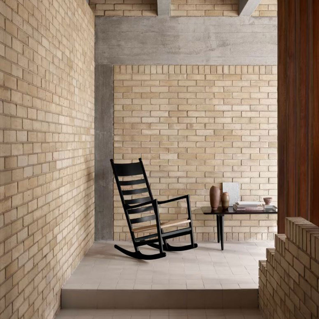 Black wooden rocking chair on a light stone floor, surrounded by textured beige brick walls and warm wooden accents.