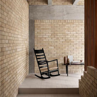 Black wooden rocking chair on a light stone floor, surrounded by textured beige brick walls and warm wooden accents.