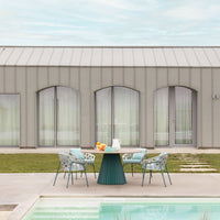 "Outdoor dining set with teal chairs featuring floral patterns, round green table, and a serene poolside view."