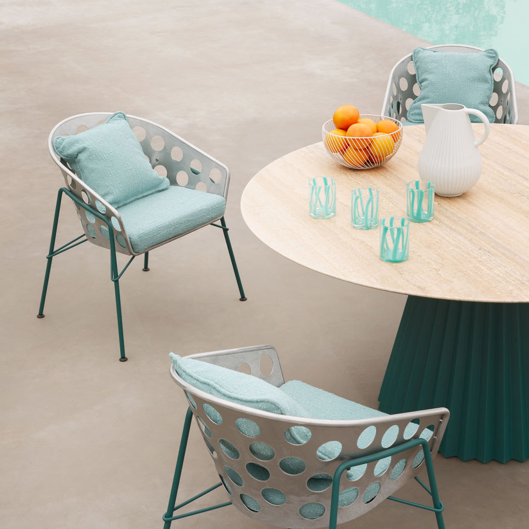 A mint green patio set with circular hole patterns, paired with a round wooden table and turquoise glassware.