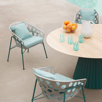 A mint green patio set with circular hole patterns, paired with a round wooden table and turquoise glassware.