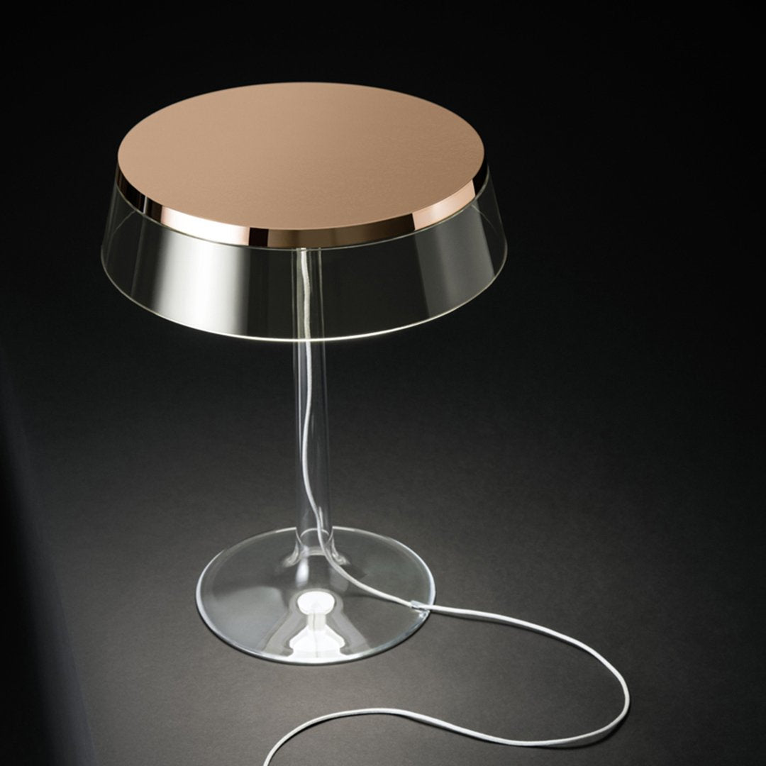 Modern lamp with a reflective bronze top and clear base, showcasing a sleek, minimalist design against a dark background.