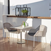 Two gray wicker chairs with white accents around a white table, set against a minimalistic white background.