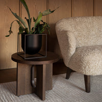 "Textured cream chair, dark wood table, and sleek black planter contrast against warm wood paneling and a neutral rug."