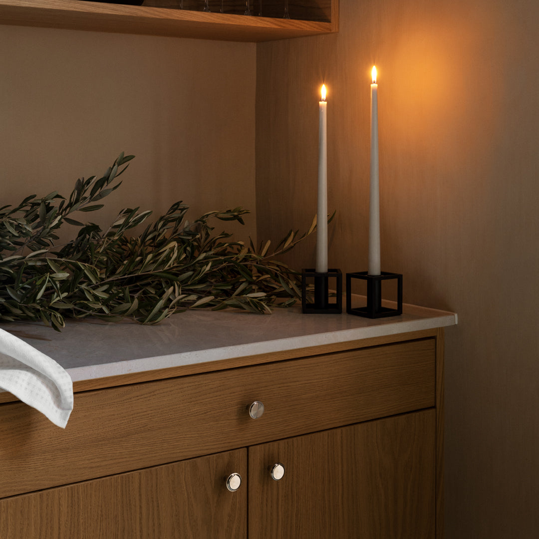 "Elegant white candles in black holders, complemented by green olive branches on a warm wooden surface."
