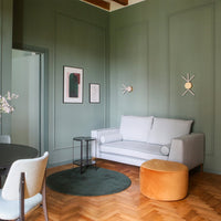 Gray sofa, mustard ottoman, green rug, and earthy green walls in a modern interior setting with geometric wall decor.