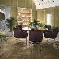 Elegant purple velvet chairs surround a round table, set against gold-patterned walls and natural wood flooring.