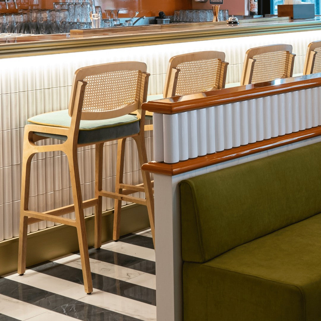 "Modern wooden bar stool with a light green seat against a backdrop of sleek black and white striped flooring."