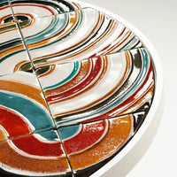 Colorful ceramic plate featuring vibrant swirls of red, orange, teal, and white patterns. Unique decorative design.