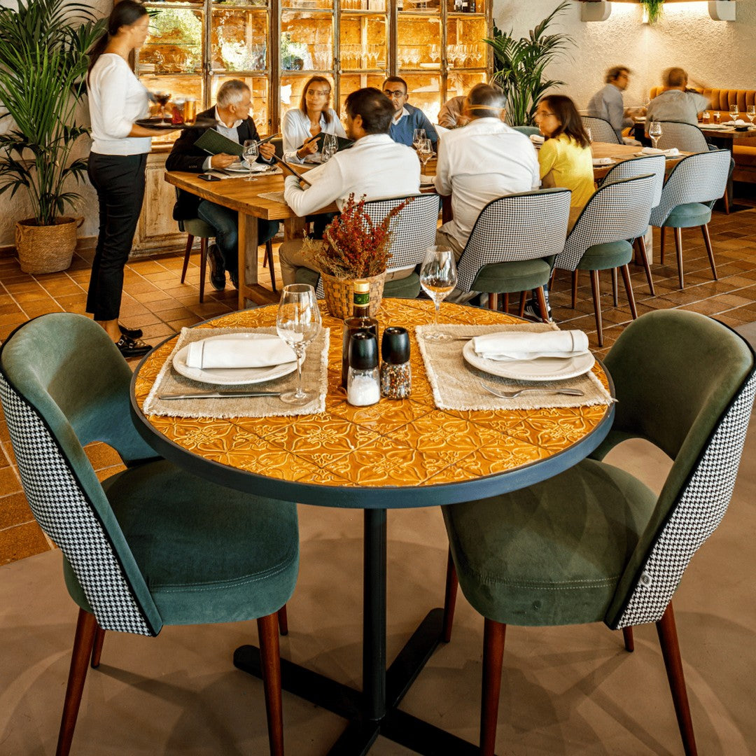 "Round table with a patterned wood top, paired with green and textured gray chairs in a vibrant dining setting."
