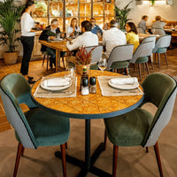 "Round table with a patterned wood top, paired with green and textured gray chairs in a vibrant dining setting."