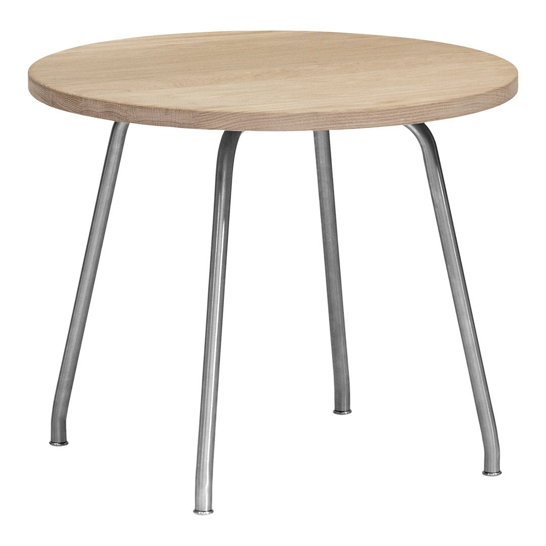 Round wooden table with a light oak surface and sleek silver legs, featuring a minimalist design.