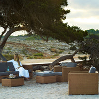 Cozy outdoor seating set featuring gray cushions and wicker details, set against a natural sandy beach backdrop.