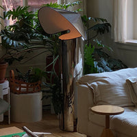 Sleek silver lamp with a curved shade, contrasting with lush green plants and neutral-toned furniture for a modern look.