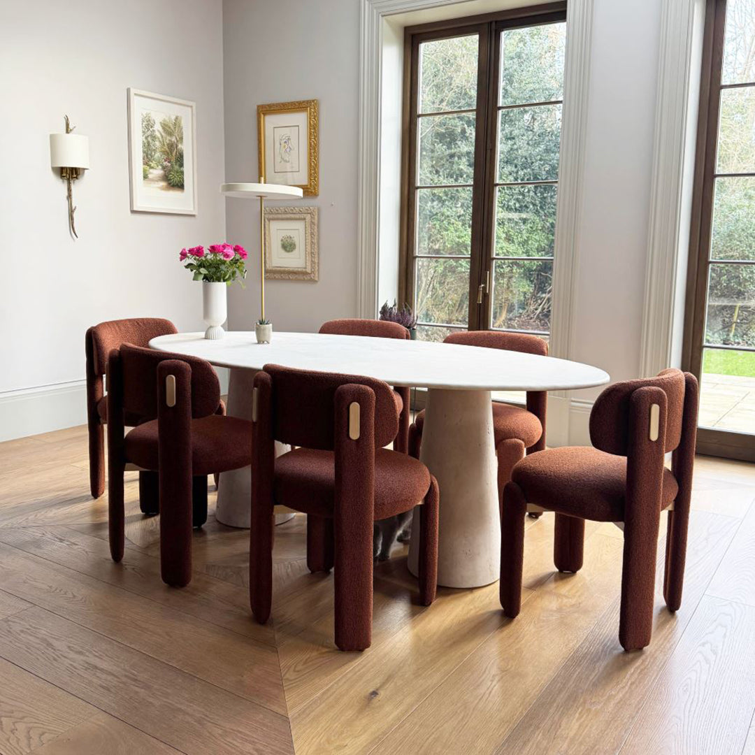 Brown upholstered chairs surround a white oval table, set on warm wood flooring, in a stylish interior.