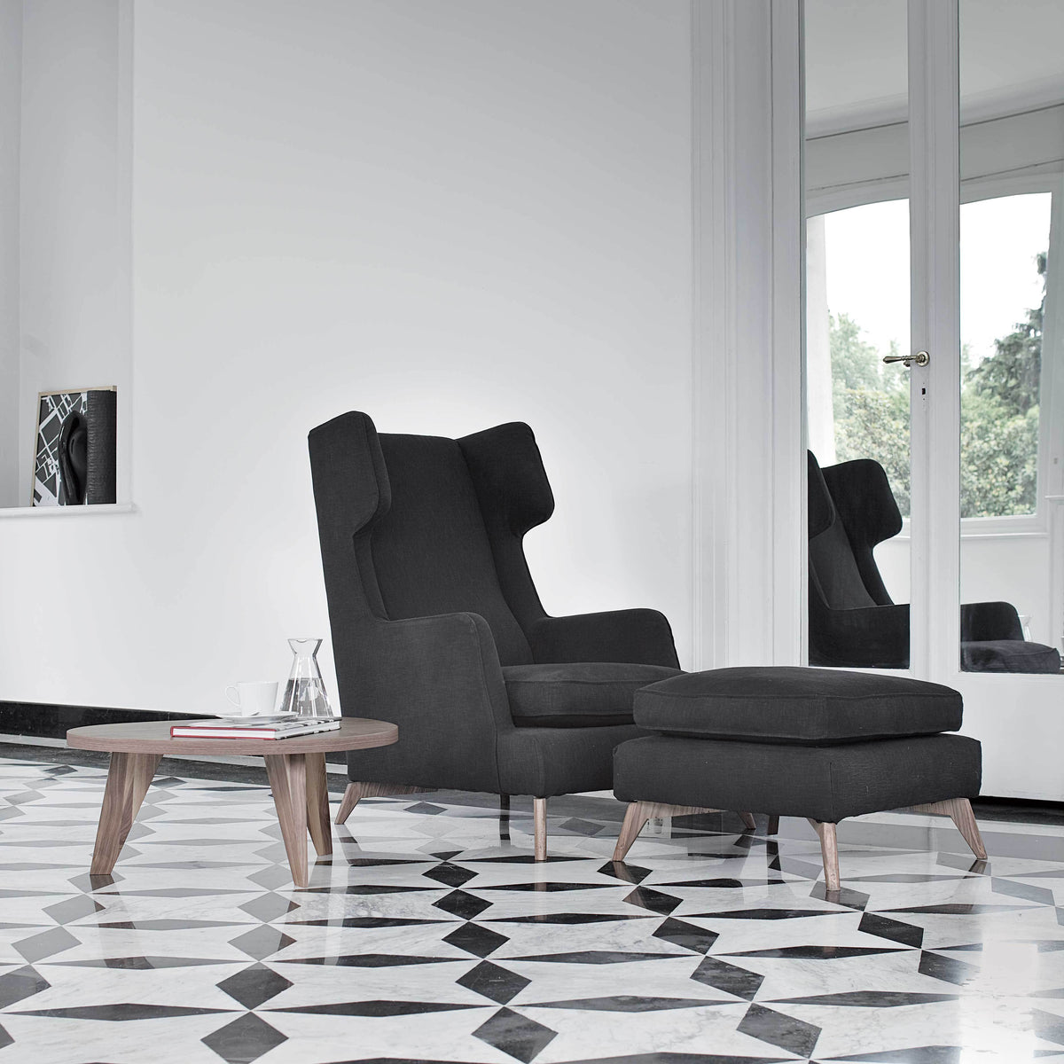 Gray upholstered chair with matching ottoman, set against a black and white geometric patterned floor.