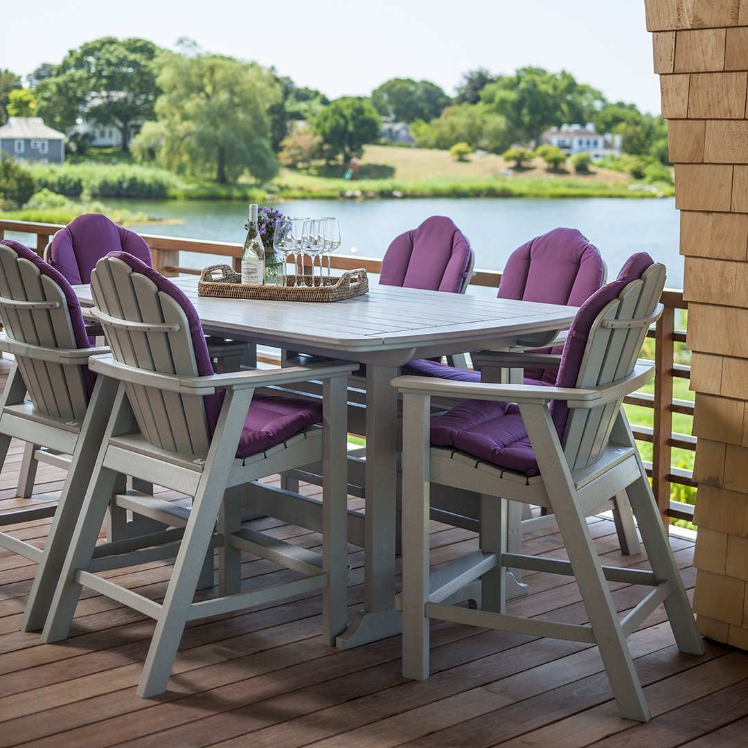 Gray outdoor table with purple cushioned chairs, set against a scenic lakeside view.