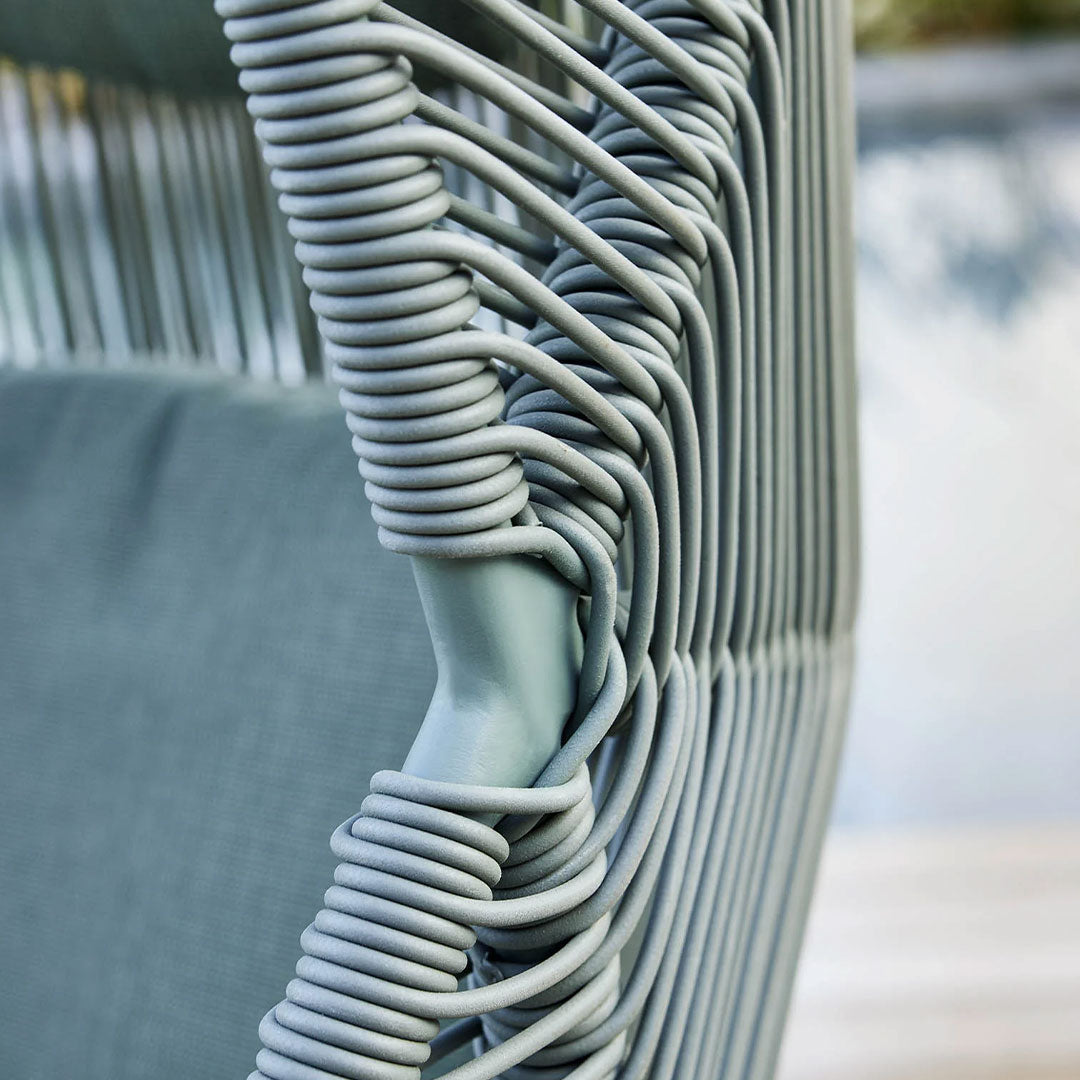 "Coiled light blue rope detail on a stylish outdoor chair with a soft gray cushion."